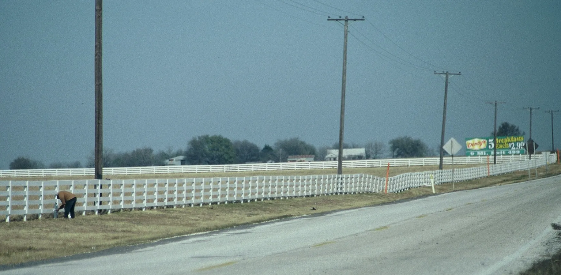 Man, bent over, painting an near endless looking board fence